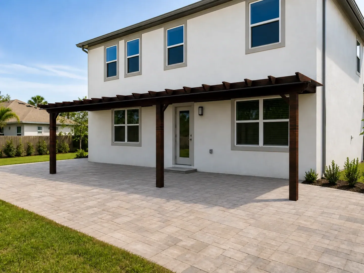 Visualización de una pérgola de madera oscura sobre la terraza pavimentada de una casa blanca.